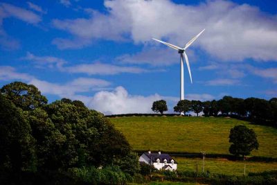 Wind turbine on a top of a hill with white house in the foreground.