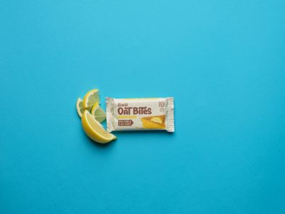 Lemon bake oat bites in packaging with slice of lemon and blue background