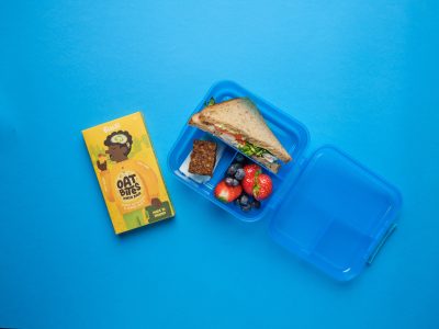 Blue lunchbox with sandwich, fruit and lemon cake oat bite with multipack box beside it