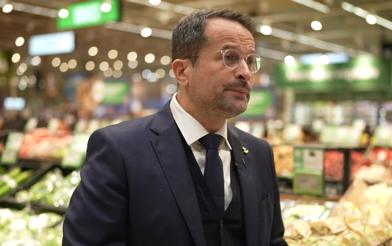 A spokesperson from an international supermarket train speaks, with supermarket environment in background.